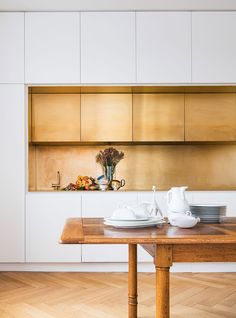 a table with plates and cups on it in front of a kitchen counter top that has white cupboards