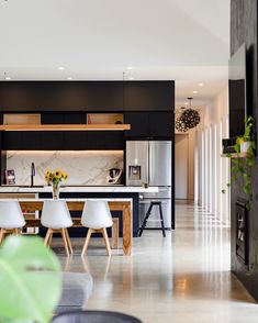 an open kitchen and dining area with white chairs, black cabinets and marble countertops