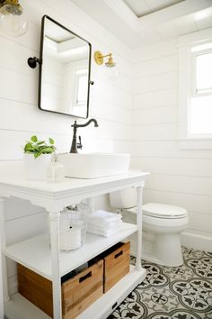 a white bathroom with black and white tile flooring, a sink, toilet and mirror