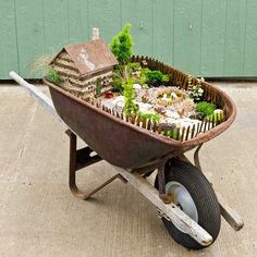 a wheelbarrow filled with miniature garden plants and small house in the back yard