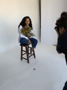 a woman is sitting on a stool with flowers in her hand and taking a photo