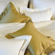 a bed with white sheets and gold pillows