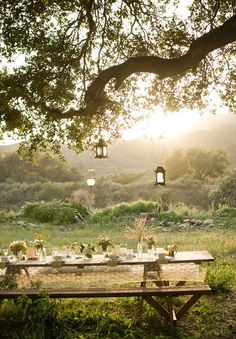 a picnic table is set up in the middle of a field with lanterns hanging above it