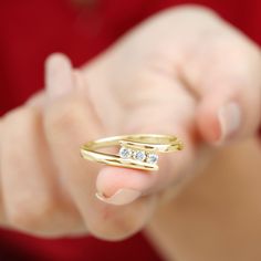 a woman is holding out her gold ring with two diamonds