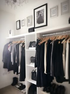 a white closet with clothes and shoes hanging on the wall next to it is a chandelier