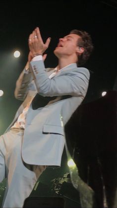 a man in a suit and tie standing on stage with his hands up to the sky