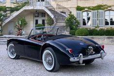 an old fashioned black sports car parked in front of a large building with steps leading up to it