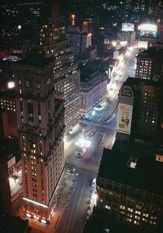 an aerial view of a city at night with cars and buildings in the foreground