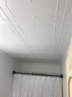 a bathroom with white walls and ceiling tiles on the ceiling, along with a shower curtain