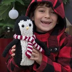 a young boy holding a knitted penguin in front of a christmas tree with ornaments