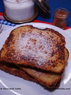 two pieces of french toast on a white plate with powdered sugar over them and a glass of milk in the background