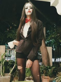 a woman with makeup on her face standing in front of potted plants