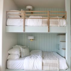 two bunk beds with white linens and pillows on them in a room that has light blue walls