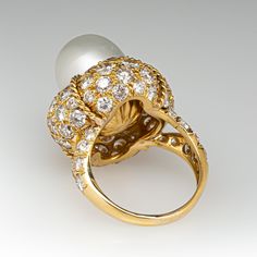 This magnificent cocktail ring is centered with one (1), post set, cultured South Sea pearl. The pearl tops a domed setting is bead set sixty-four (64), bead set, round brilliant cut diamonds. The ring has a split shank design and is accented with seven (7), bead set, round brilliant cut diamonds on each side. The ring measures 21.7mm at the top, rises 18.6mm above the finger, tapering to 2.4mm wide and 1.1mm thick at the base of the shank. The ring is currently size 7. Elegant White Domed Rings, Elegant White Domed Jewelry, Elegant Cabochon Rings For Anniversary, Elegant White Gold Diamond Ring With Cabochon, Classic Cabochon Pearl Ring For Formal Occasions, Classic Formal Pearl Ring With Cabochon, Luxury High Luster Oval Pearl Ring, Classic Cabochon Dome Ring For Wedding, Luxury Diamond Rings With Pearl Drop