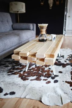 a wooden table sitting on top of a white and brown cowhide rug in front of a couch