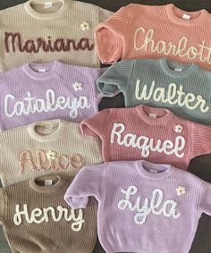 six sweaters with names on them sitting on a wooden surface, all in different colors