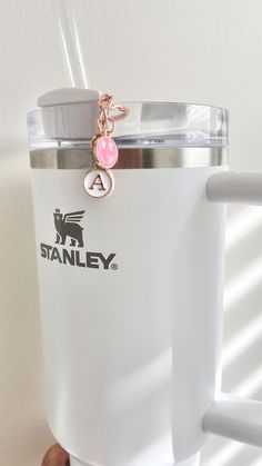 a hand holding a white coffee mug with a pink bead charm hanging from it