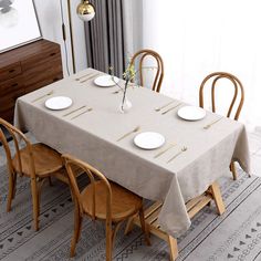 a dining room table is set with white plates and placemats, along with wooden chairs