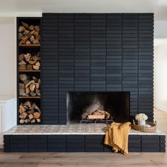 a fireplace with logs stacked on top of it in front of a black brick wall