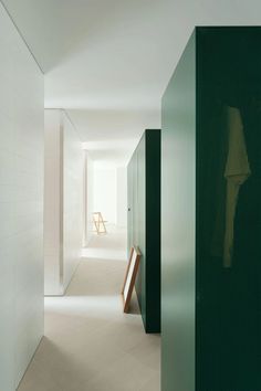 an empty hallway with white walls and green trim on the wall, leading to another room