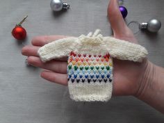 a hand holding a knitted sweater ornament next to christmas ornaments and baubles