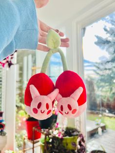 a person is holding two stuffed animals on a hook in front of a window sill