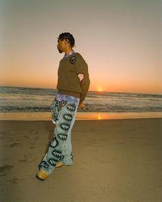 a man standing on top of a sandy beach next to the ocean at sun set