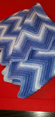 two blue and white crocheted afghans sitting on top of a red table