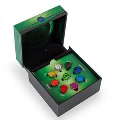 a green box with six different colored buttons in it and the lid opened to reveal its contents