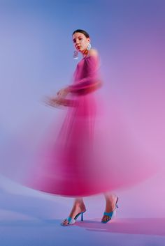 a woman in a pink dress and high heeled shoes is standing with her hand on her hip