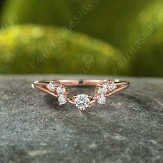 a rose gold ring with three round diamonds on the side, sitting on top of a rock