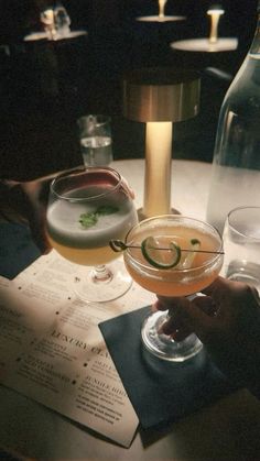 two people are holding wine glasses at a table with menus and drinks in front of them