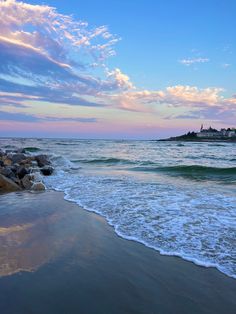 the ocean waves come in to shore as the sun goes down over an island and houses