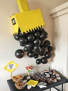 a table topped with lots of black and yellow balloons next to a sign that says happy birthday