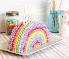 a rainbow cake on a plate next to some strawberries and candy sticks in a jar