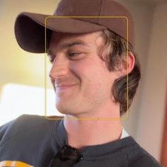 a man wearing a brown hat and smiling at the camera with a square frame over his face