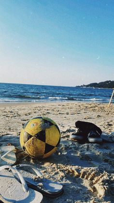 a yellow soccer ball sitting on top of a sandy beach next to flip flops