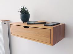 a wooden shelf with a cell phone on it next to a radiator and a potted plant