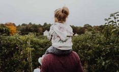 a woman holding a child in her arms while walking through an apple orchard with lots of trees