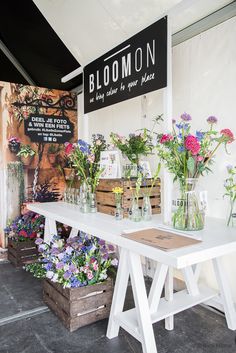 a white table topped with lots of vases filled with purple and pink flowers next to a sign