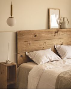 a bed with white linens and wooden headboard next to a lamp on the wall