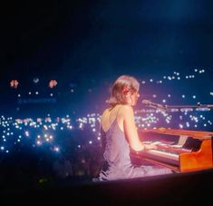 a woman sitting at a piano in front of a microphone with lights on the background