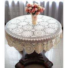 a vase with flowers is on top of a round doily tablecloth in front of a window