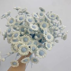 a bouquet of white and blue crocheted flowers in someone's hand on a gray background