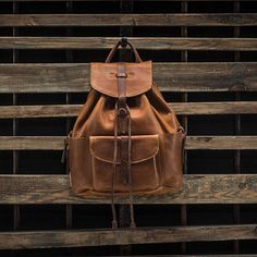 a brown leather backpack hanging on a wooden wall