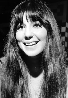 a black and white photo of a woman with long hair smiling in front of a wall