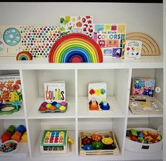 children's toys and books on shelves in a playroom with rainbows painted on the wall