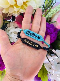 a person's hand holding two beaded bracelets with the word mom on them