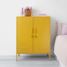 a yellow locker next to a bed with pink pillows and flowers on the top shelf