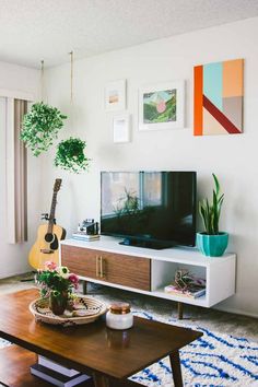 a living room with an entertainment center, guitar and potted plants on the coffee table